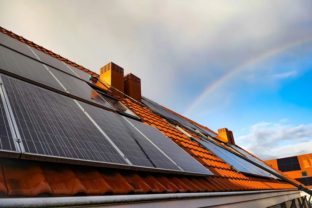 Solar panels on an orange tiled roof with a rainbow in the sky
